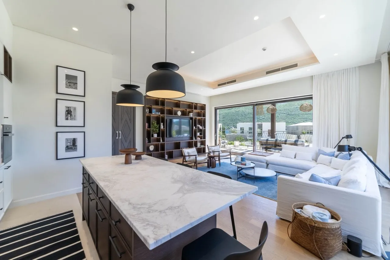 Modern living room featuring a white sofa, marble kitchen island, and a large wooden shelving unit with a TV.