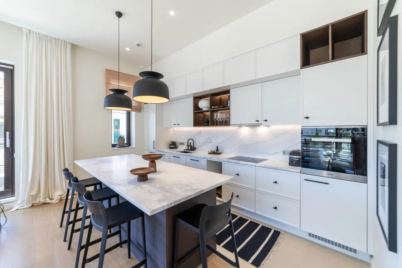 Modern kitchen with white cabinets, a marble island, black bar stools, and pendant lights over the counter.