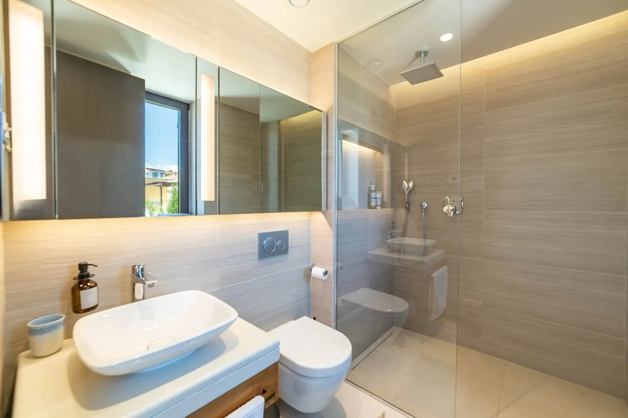 Modern bathroom featuring a vessel sink, wall-mounted toilet, and glass-enclosed shower with beige tiled walls.