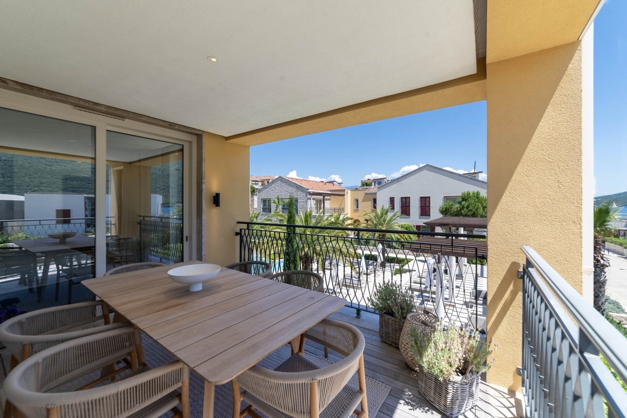 Spacious terrace with dining area in an apartment in Portonovi, Kumbor, Montenegro: resort view and panoramic glazing.
