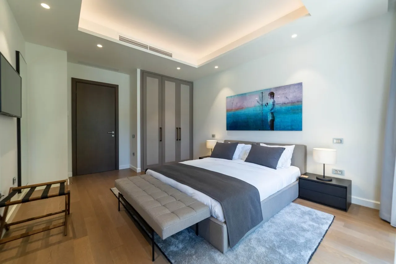Modern bedroom featuring a double bed with gray headboard, nightstands, luggage rack, and large blue artwork on the wall.
