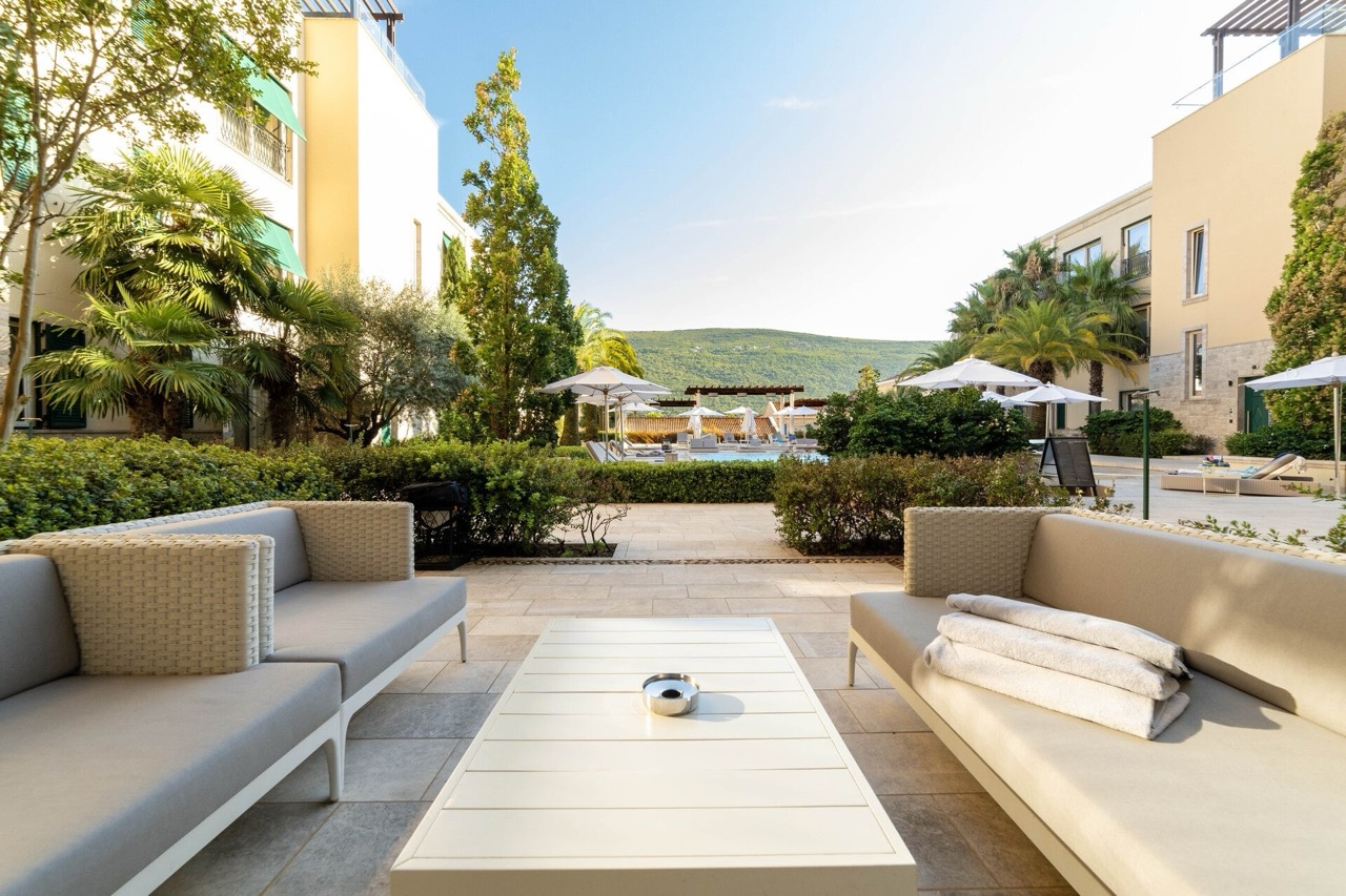 Terrace with soft seating and a view of the pool and mountains in the Portonovi residential complex, Kumbor, Montenegro.