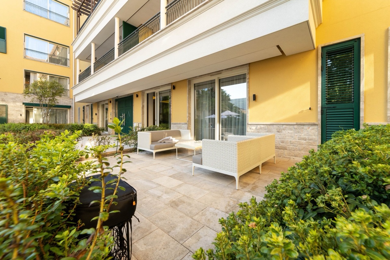 Terrace with wicker furniture at the apartments in the Portonovi complex, Kumbor, Montenegro: view of a residential building with a garden.