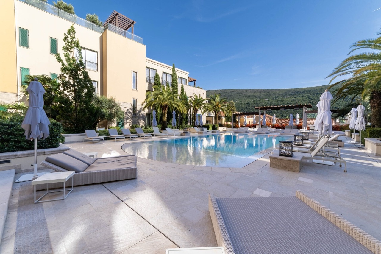 Outdoor swimming pool with sun loungers in the Portonovi residential complex, Kumbor, Montenegro: view of the terrace and mountains.