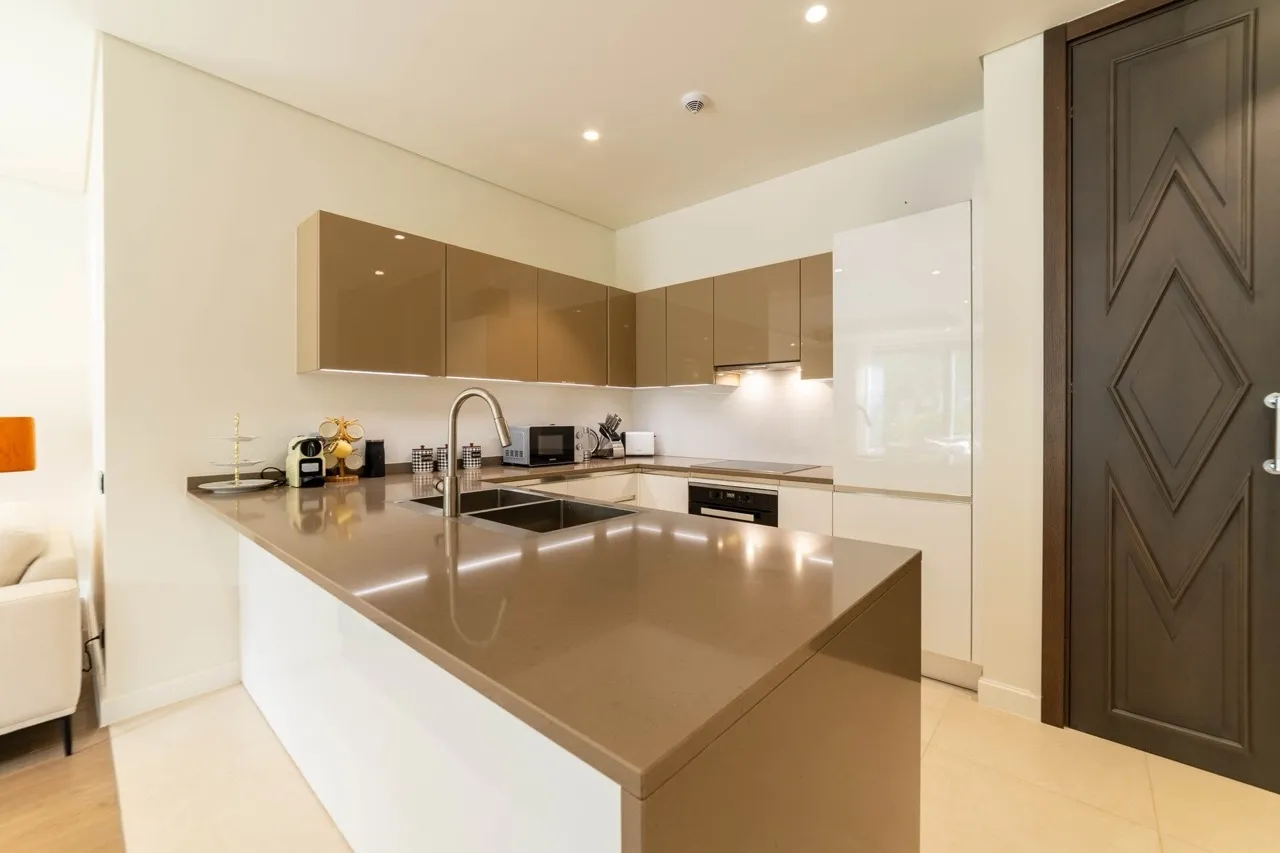 Modern kitchen with a central island, glossy beige cabinets, sink, and built-in appliances.