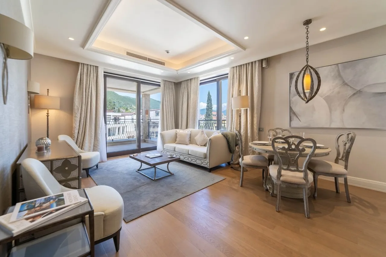 Living room with a white sofa, coffee table, and dining set near large windows overlooking hills.