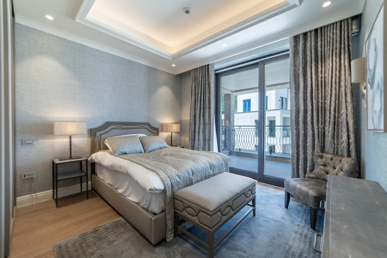 Modern bedroom featuring a double bed, nightstands, an upholstered bench, and sliding glass doors leading to a balcony.