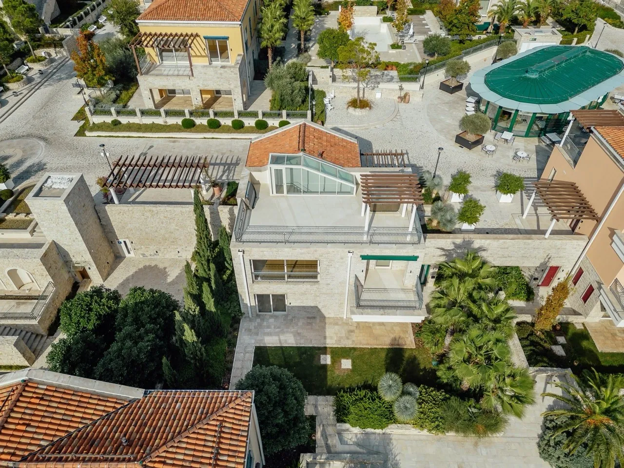 Aerial view of a stone building with terracotta roof, gardens, pergolas, and a pavilion with a green dome.