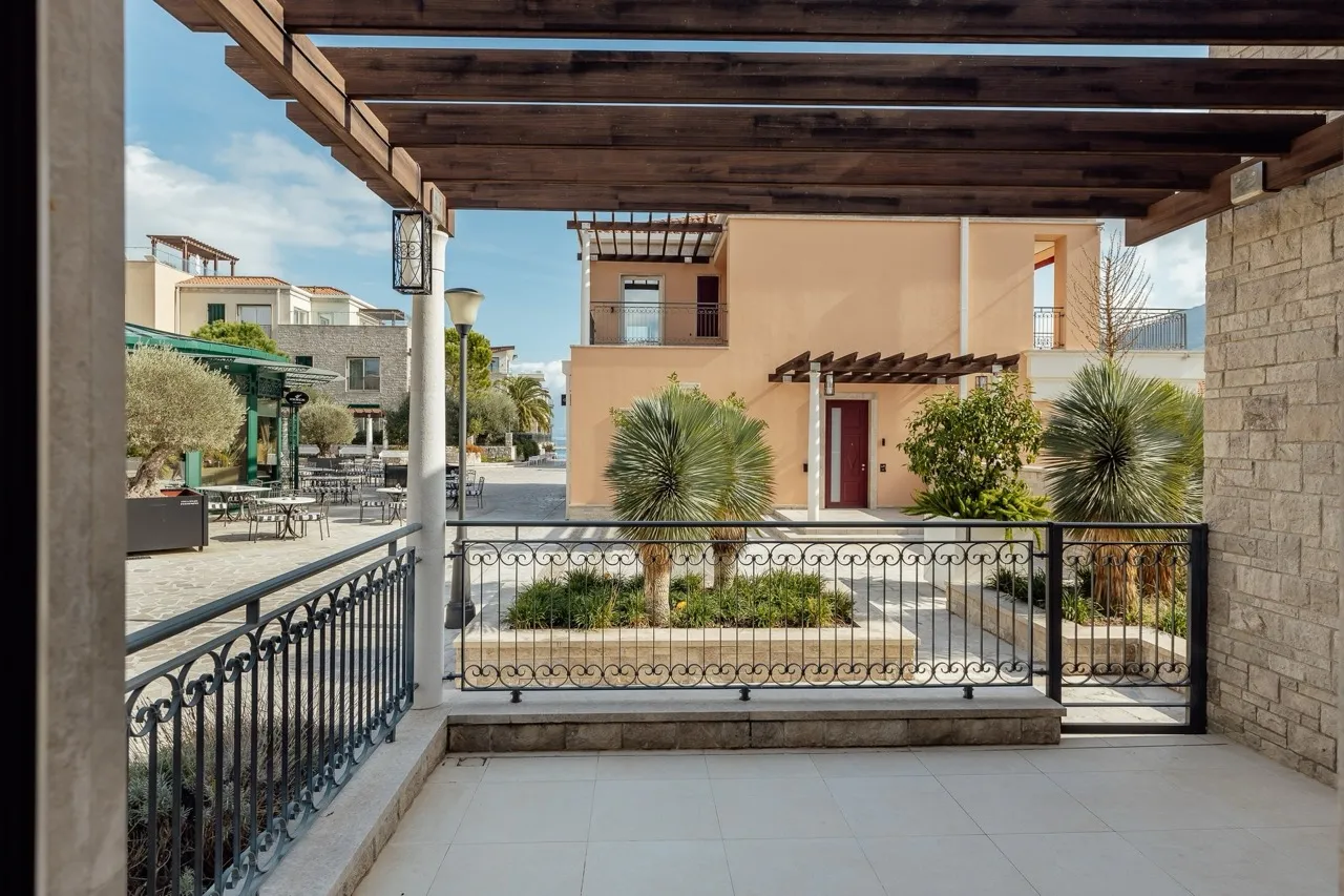 View from a balcony with a wooden pergola and wrought iron railing overlooking buildings and plants.