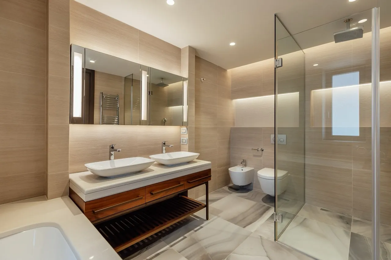 Modern bathroom featuring double vessel sinks, glass shower enclosure, and beige tiled walls.