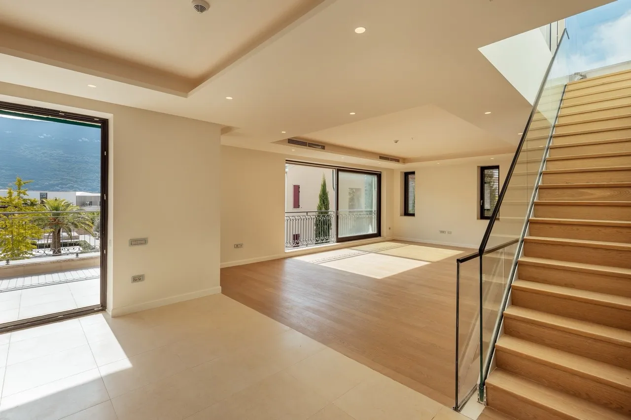 Empty room with wooden flooring, glass staircase railing, and sliding doors leading to a balcony with sea view.