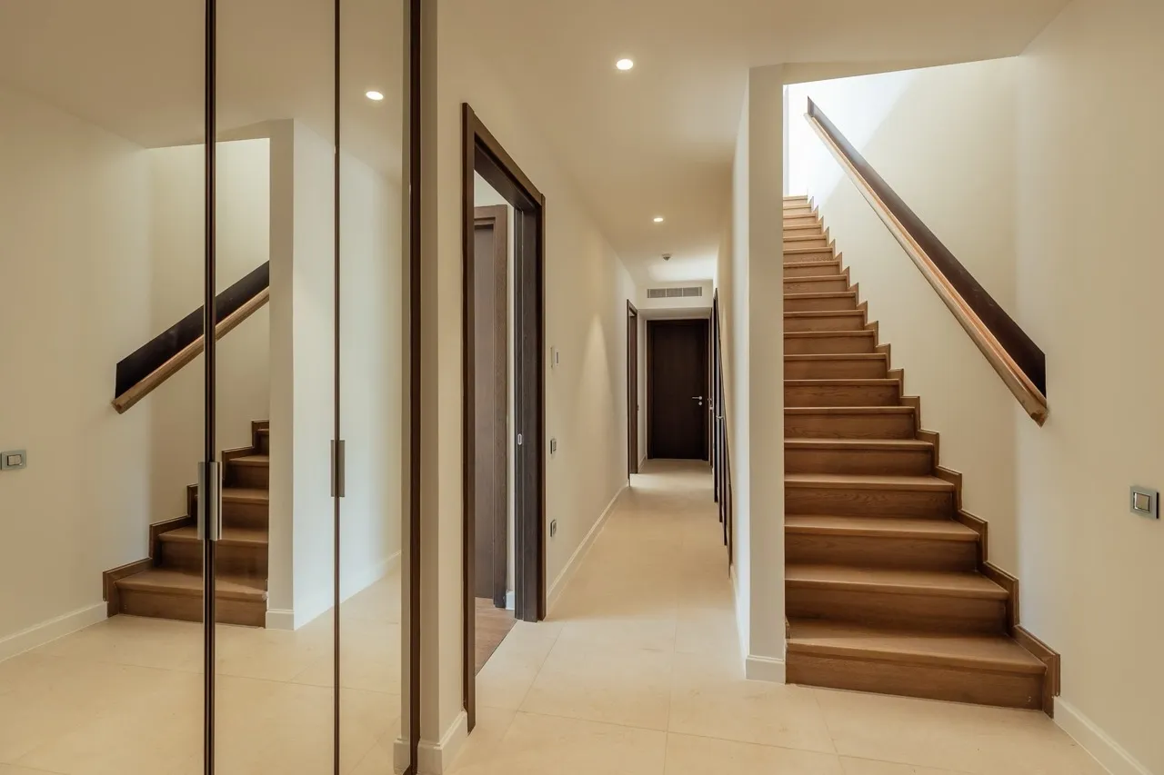 Bright hallway with wooden stairs and a mirrored wall leading deeper into the residence.