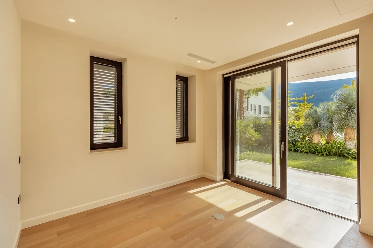 Empty room with wooden flooring and large glass doors opening to a garden view.
