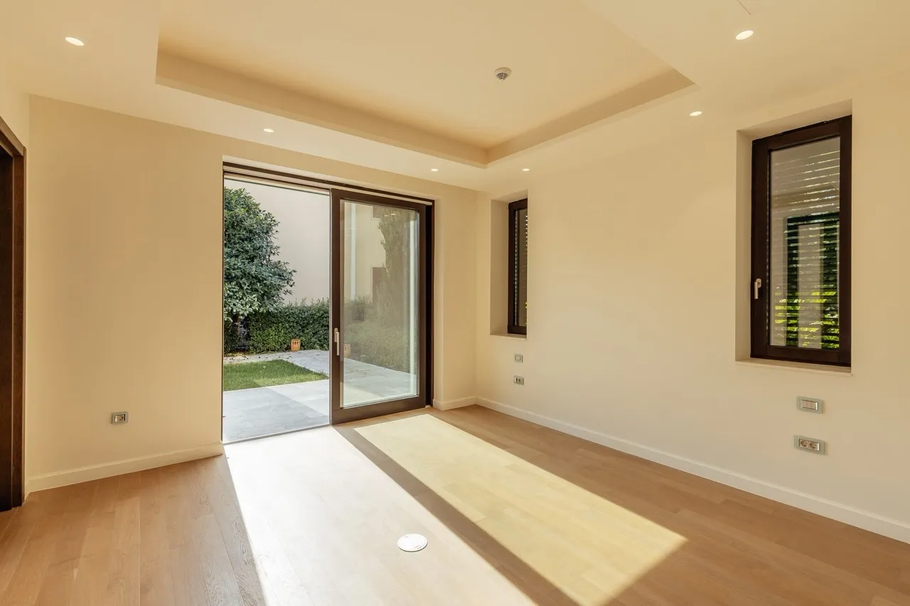 Empty room with wooden flooring, large sliding glass door opening to a garden.