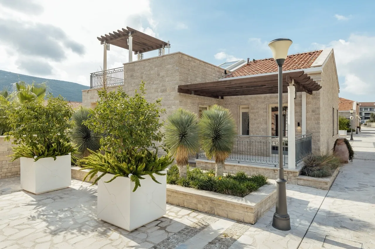 Stone house exterior with terrace, white planters, and landscaping against a mountain backdrop.