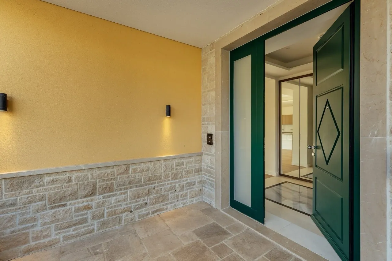 Entrance area with a yellow wall, stone cladding, and an open green door leading inside.