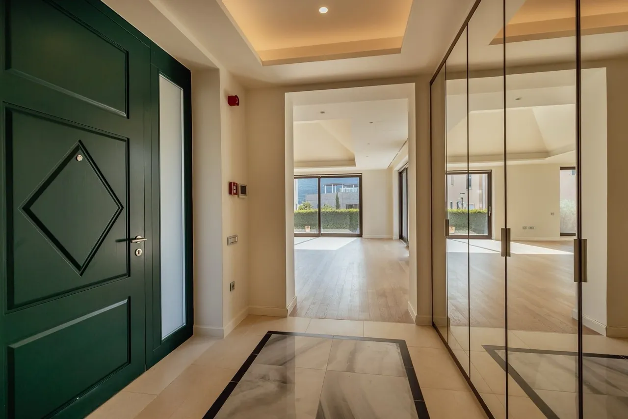 Entryway featuring a dark green door, marble tile floor with black border, and glass walls.