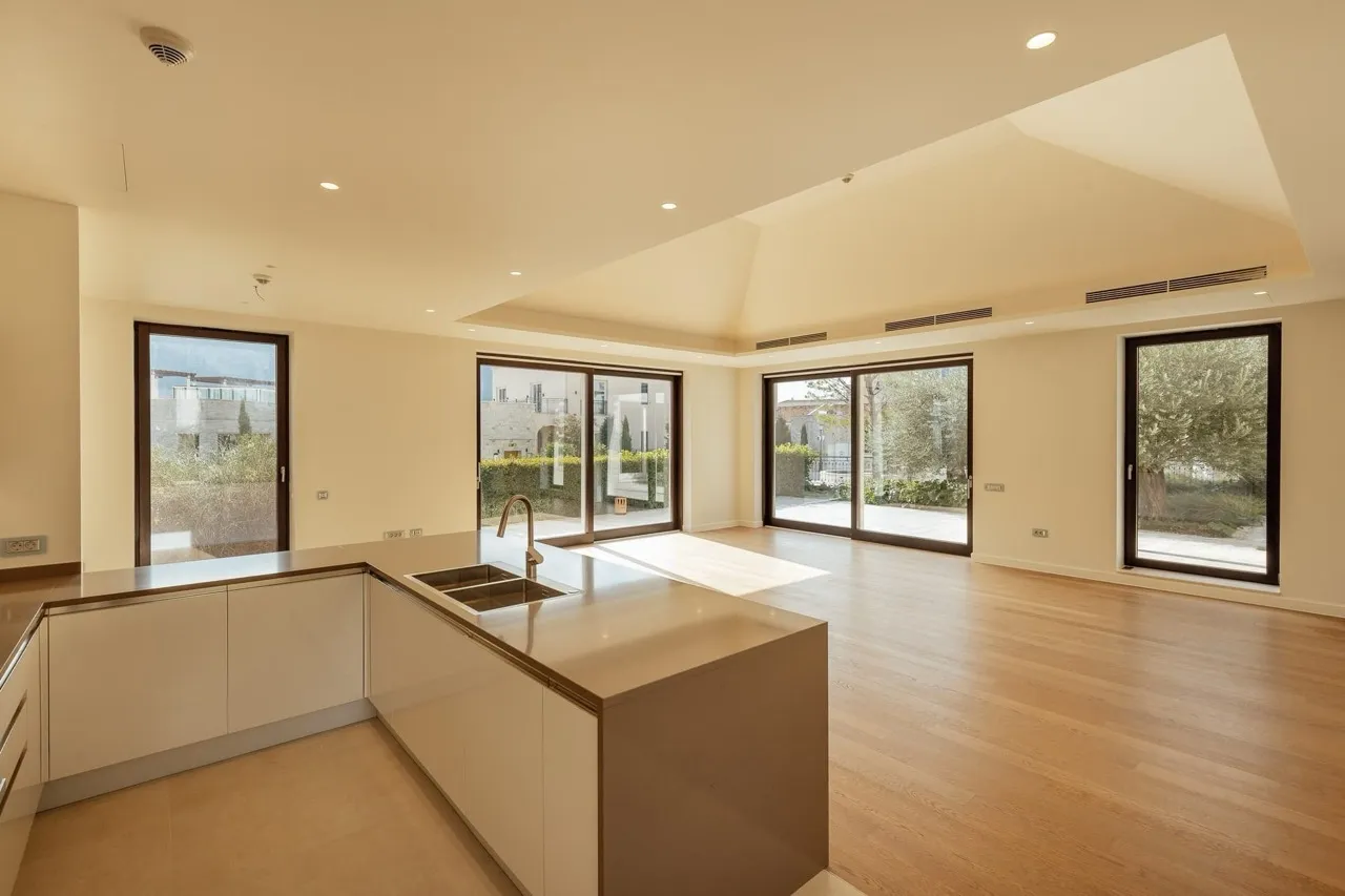 Modern kitchen with a white island, sink, and faucet, featuring wood flooring and large windows.