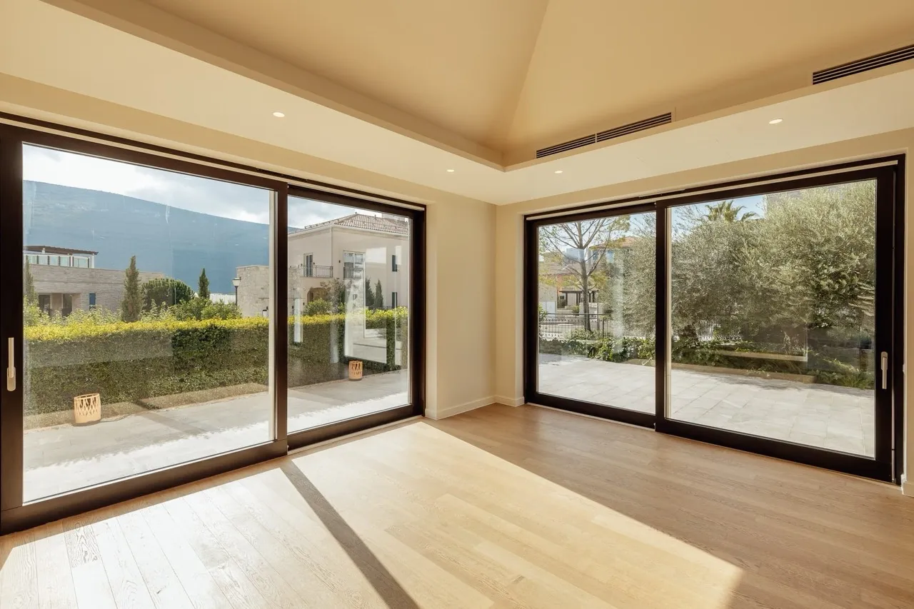 Empty room with light wood flooring and large sliding glass doors opening to a garden view.