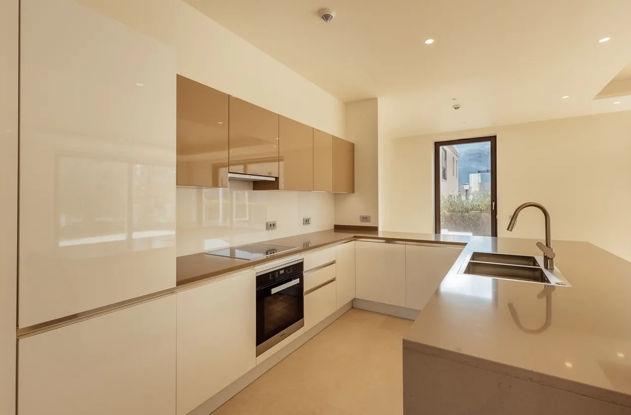 Modern kitchen featuring beige glossy cabinets, built-in oven, cooktop, and a sink on the central island.