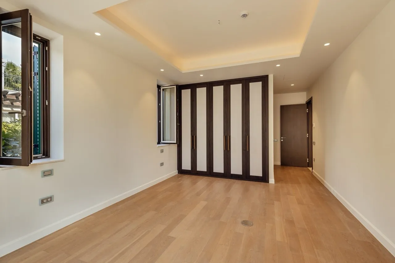 Empty room with wooden flooring, built-in wardrobe with dark frames, and a window overlooking outside.