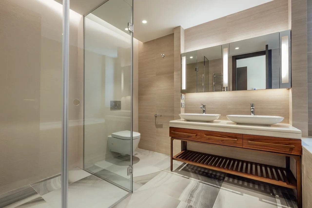 Modern bathroom featuring a double vessel sink on a wooden vanity, glass shower enclosure, and wall-hung toilet.