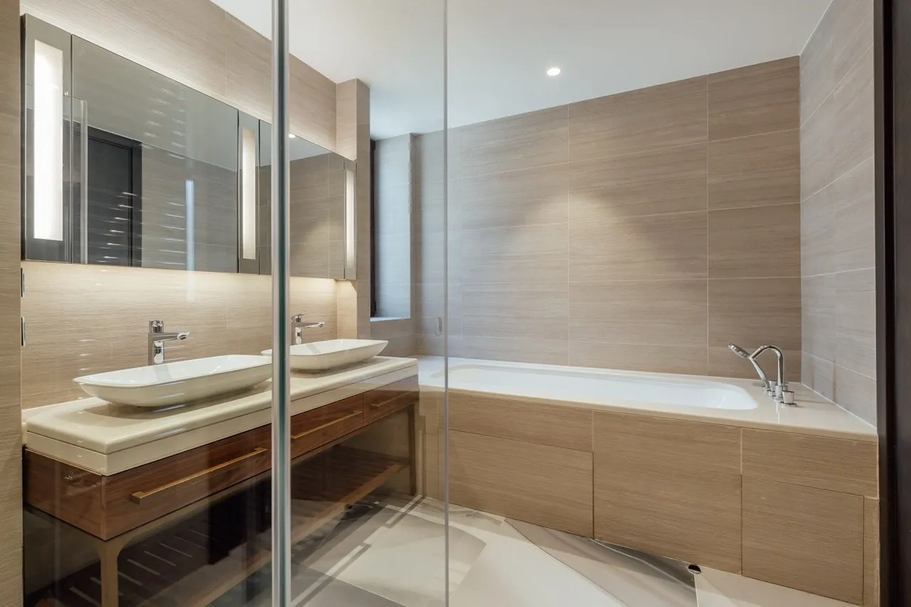 Modern bathroom featuring a double vessel sink on a wood vanity and a large built-in bathtub with beige tiles.