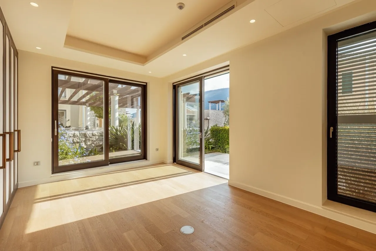 Empty room with hardwood floors and large glass doors opening to a garden, typical living area.