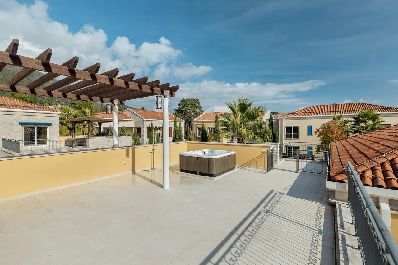 Open terrace featuring a hot tub, wooden pergola, and views of neighboring houses under a blue sky.