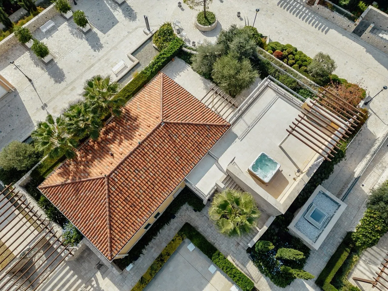 Aerial view of a terracotta tiled roof, terrace with a hot tub, and landscaped garden with palm trees.