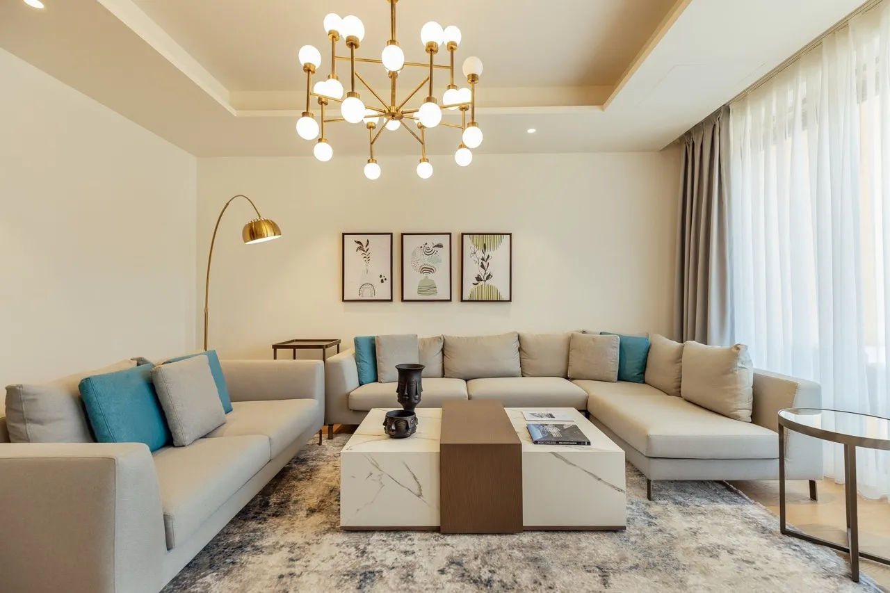Bright living room with a sectional sofa, marble coffee table, gold chandelier, and wall art.
