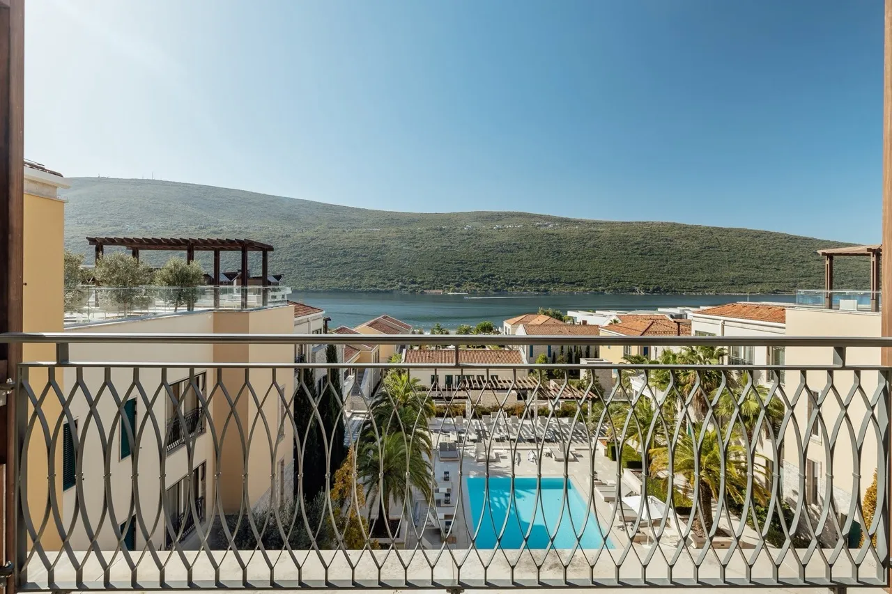 View from a balcony with metal railing overlooking a pool and sea.