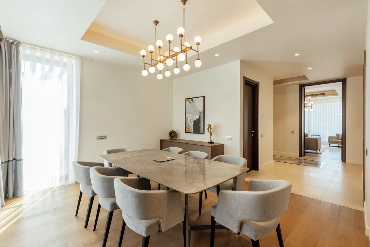 Bright dining area featuring a marble table, grey upholstered chairs, and a modern chandelier on wood flooring.