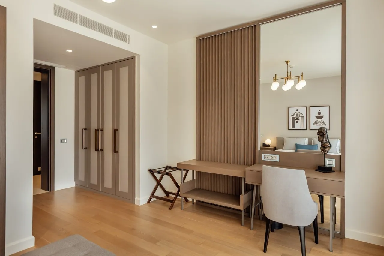 Bedroom area featuring a wardrobe, wooden desk, large mirror reflecting a bed, and a luggage rack.