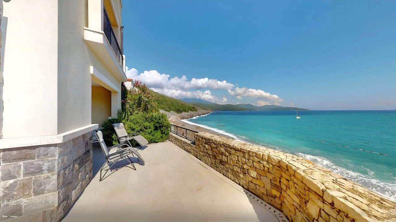 Terrace with sea view, stone wall, sun loungers, building facade on the left.