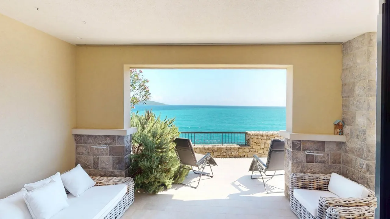 Sea-view terrace with wicker furniture, stone walls, and green shrubs under a roof.