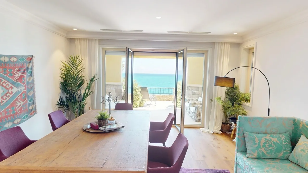 Living room with a wooden dining table, purple chairs, and a turquoise sofa facing open doors to the sea.