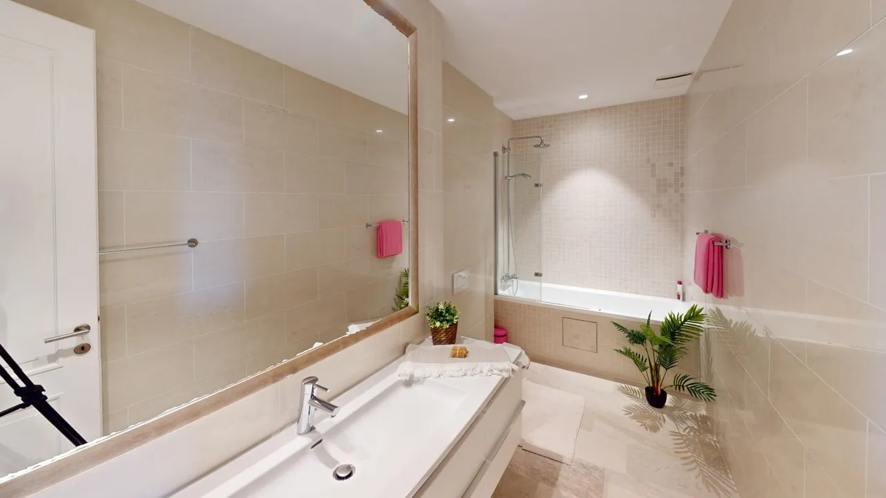 Modern bathroom featuring a white vanity sink, large mirror, bathtub, and shower area with beige tiled walls.