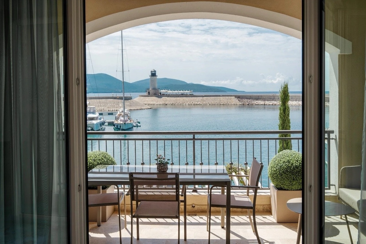 View from the apartment balcony in Luštica Bay, Radovići, Montenegro: dining area, yacht marina, and lighthouse against the sea.