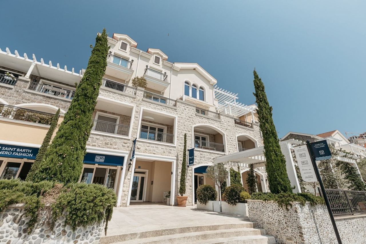 Facade of the Lustica Bay residential complex in Radovici, Montenegro: stone cladding, balconies, and shops on the ground floor.