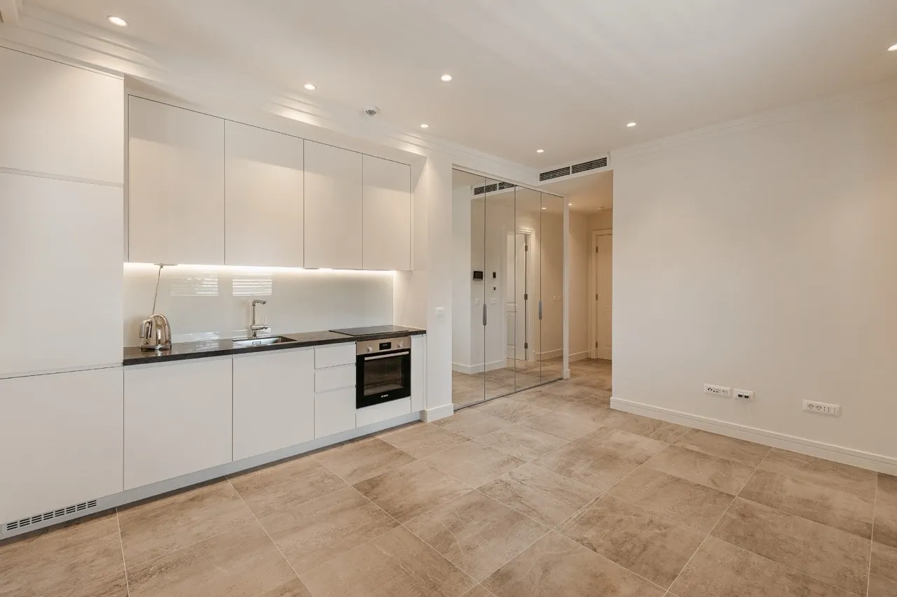 Modern kitchen with white cabinets, black countertop, sink, built-in oven, and large beige floor tiles.