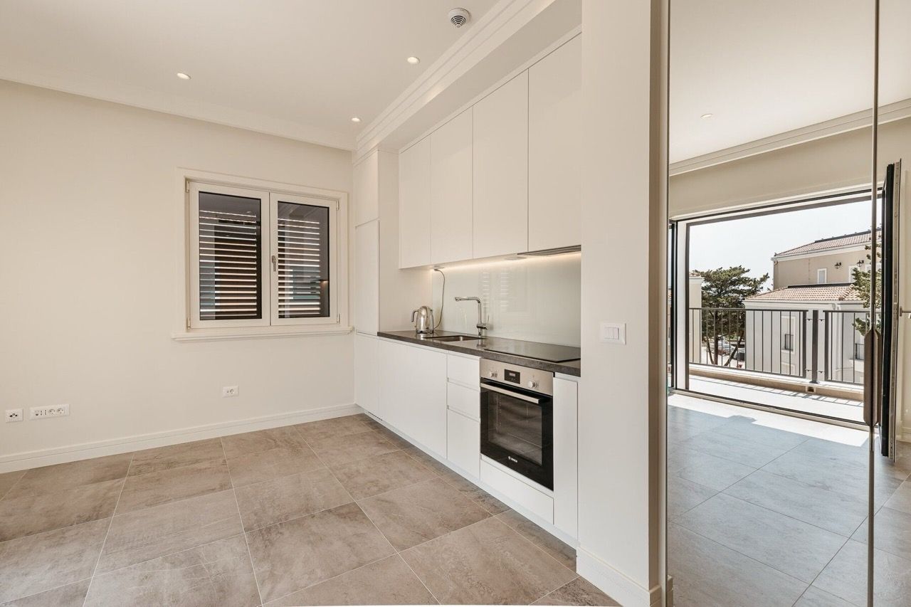 Modern kitchen with white cabinetry in an apartment at Lustica Bay, Radovici, Montenegro, with access to the terrace.