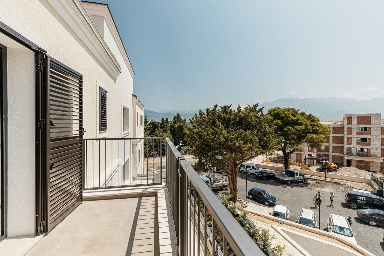 Balcony of a modern apartment in Luštica Bay, Radovići, Montenegro, with a view of the mountains and the residential complex parking area.