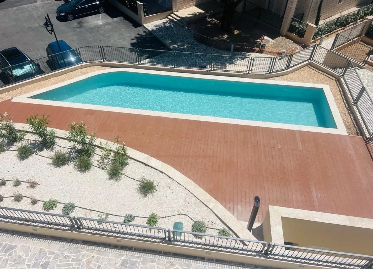 Aerial view of a blue swimming pool with a wooden deck and metal safety fencing.