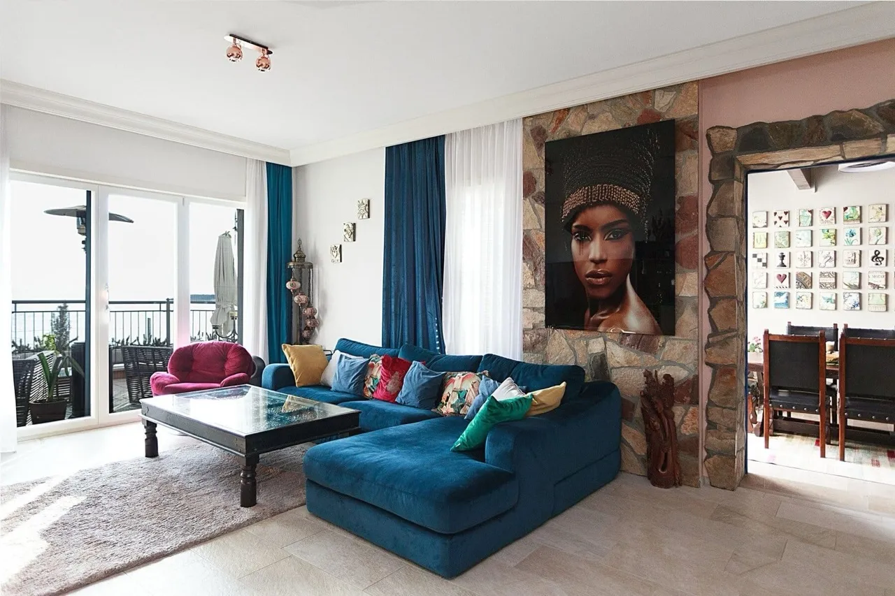 Living room featuring a blue sectional sofa, stone accent wall with large portrait, and balcony access.