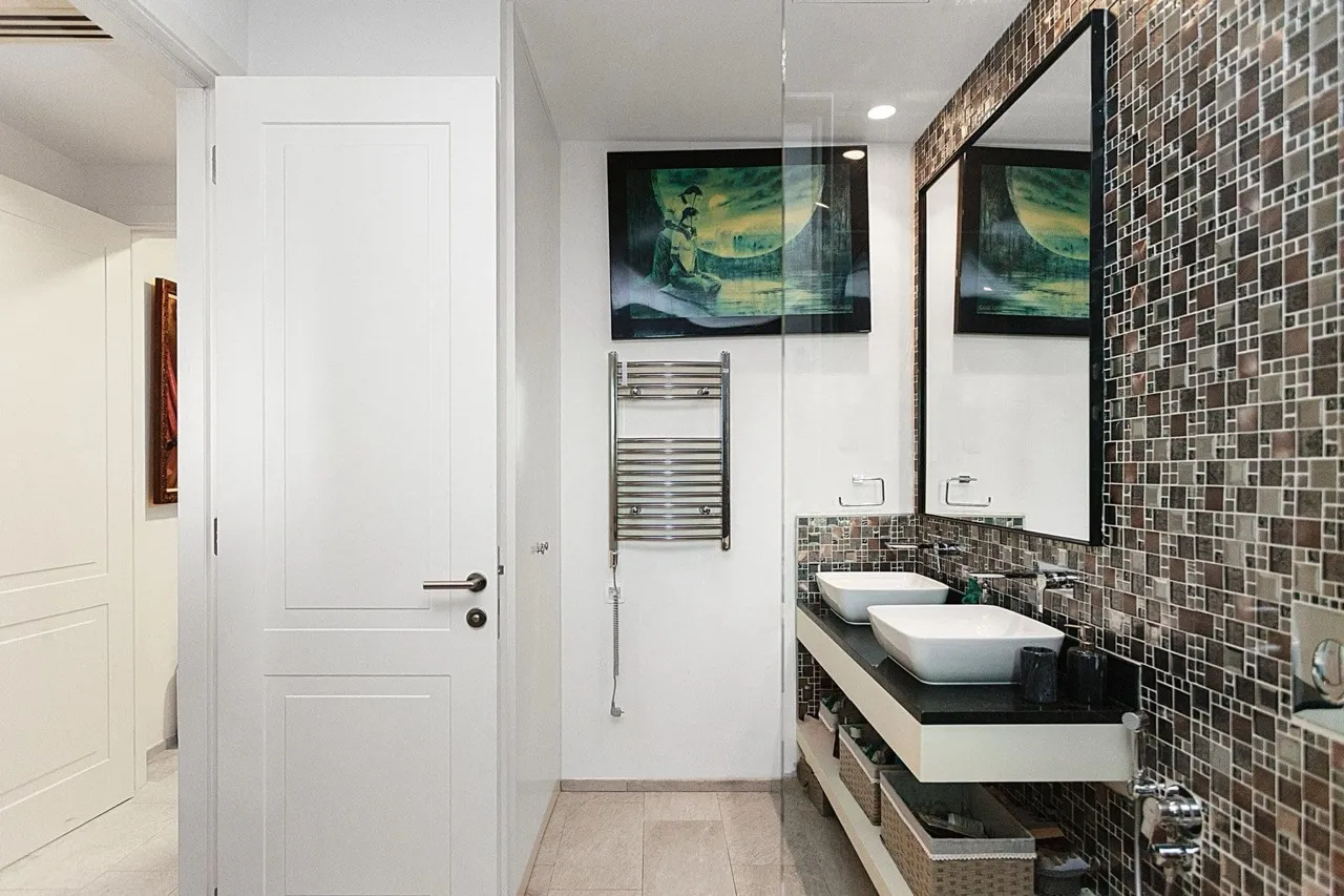 Bathroom with double sinks, mosaic wall, heated towel rail, large mirror, and glass partition.