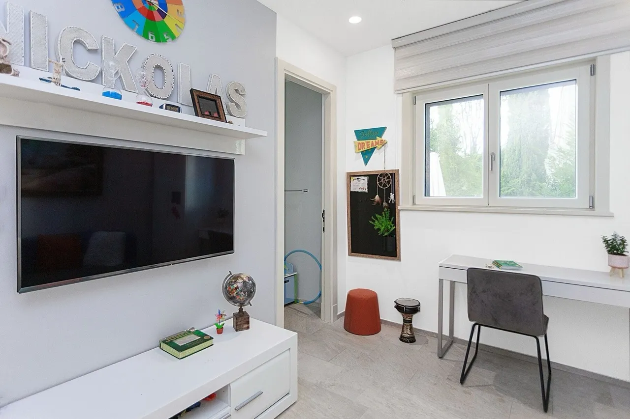 Children's bedroom featuring a wall TV, white desk, globe, and personalized name decor on the shelf.