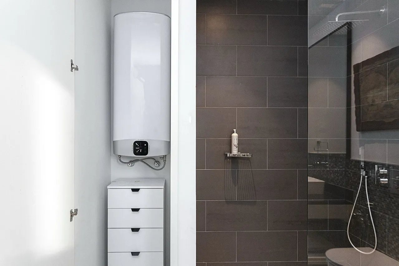 Shower with dark tiles and glass partition, white water heater, and a drawer unit visible.