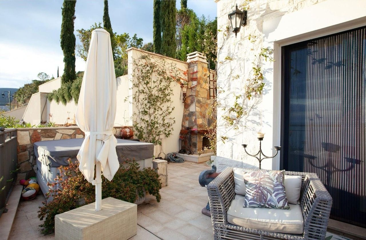Villa terrace in Luštica Bay, Radovići, Montenegro: jacuzzi, wicker chair, stone fireplace, and garden view.