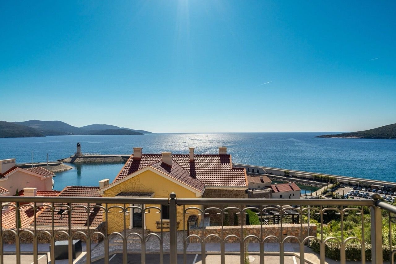 View from the villa balcony in Lustica Bay, Radovici, Montenegro: a panorama of the sea, lighthouse, and Mediterranean houses.